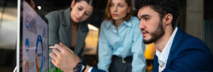 Three coworkers review data on a screen as one points during a discussion.